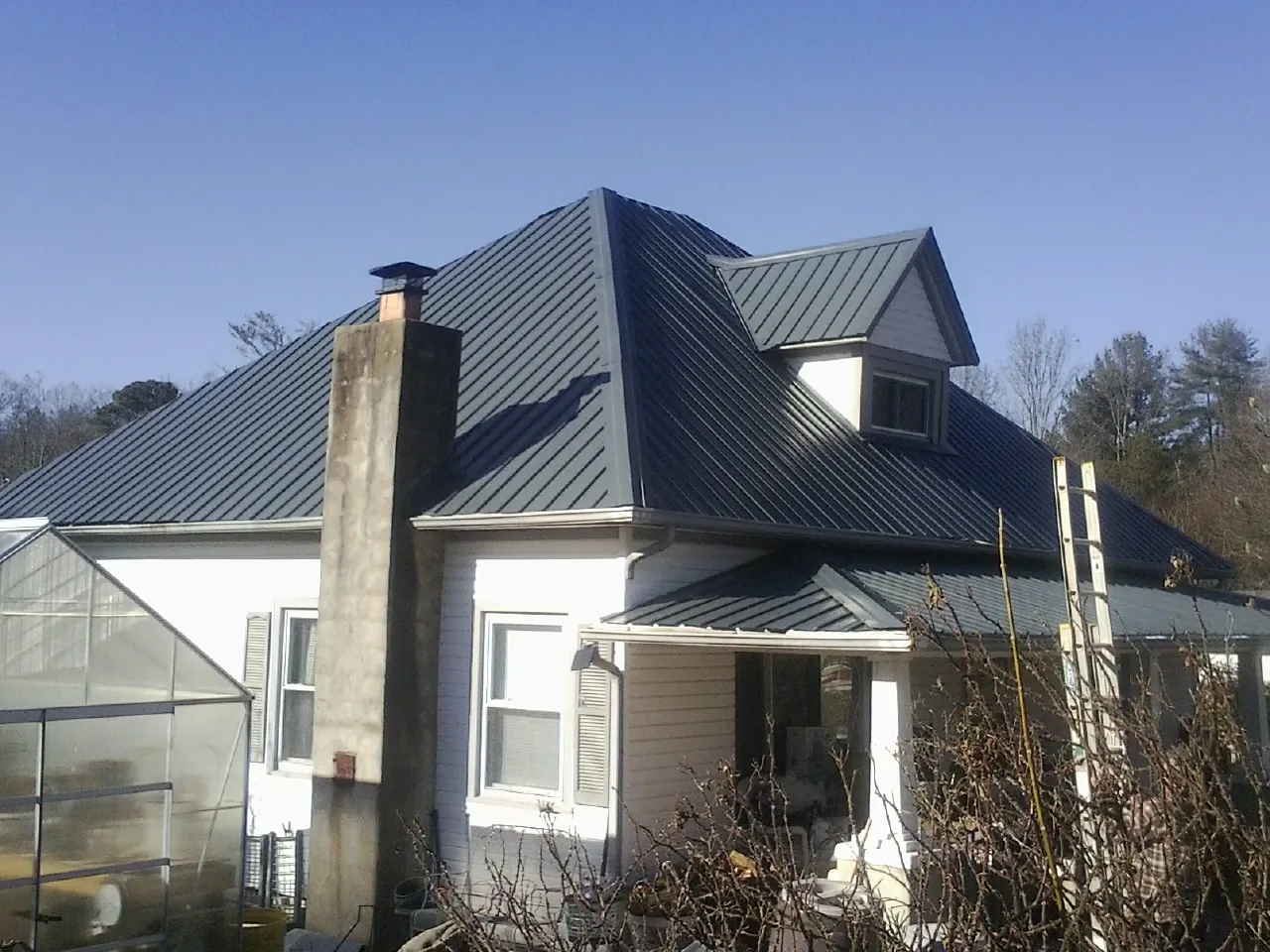 Dark blue standing seam metal roof on a white farmhouse with dormer — Slate & Tile Roof Repair by Roofing Brothers in Lyndon