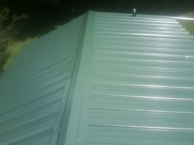 New green metal panels meeting at the ridge of a roof — Flat Roof Repair work by our crew in Lyndon