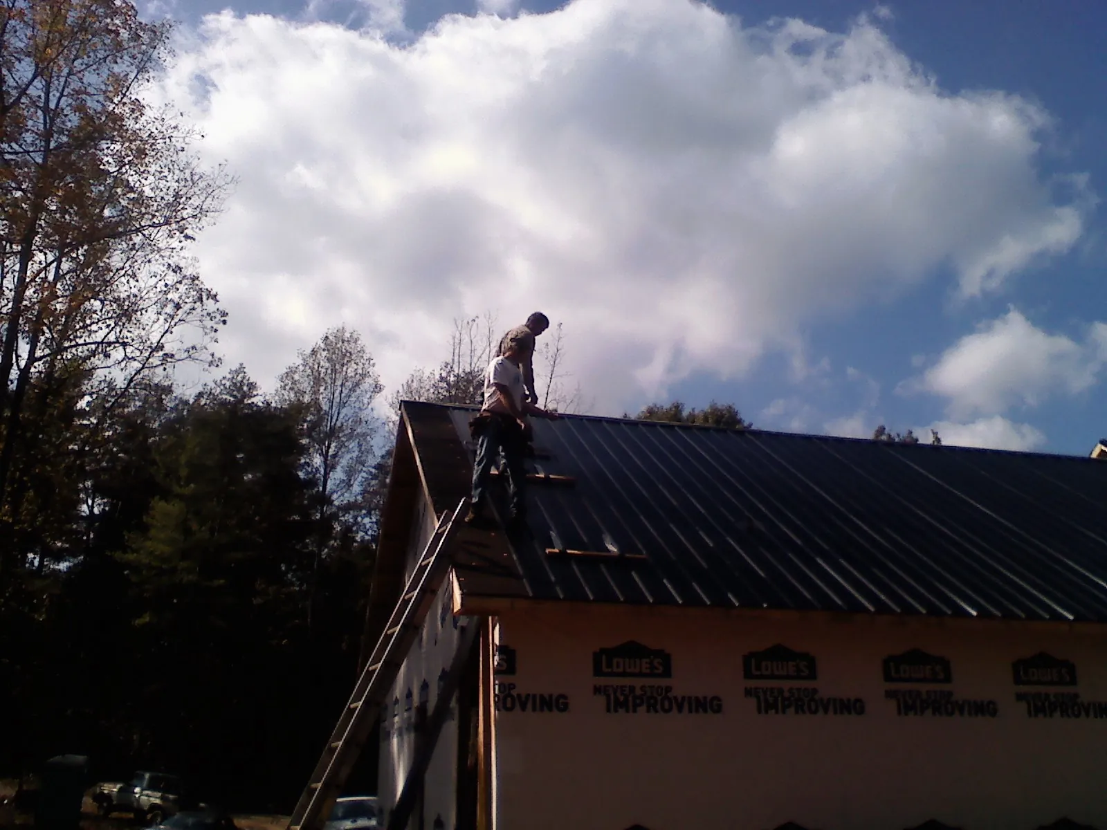 Roofer fastening dark metal panels high against a cloudy sky, from a Roof Inspection job in Lyndon