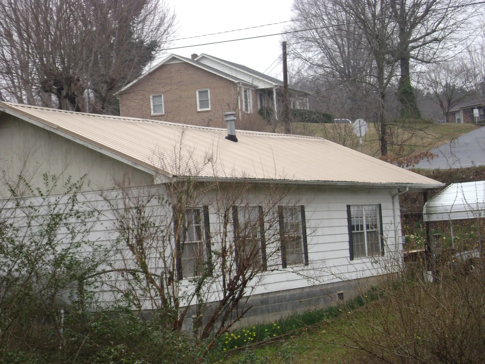 Tan metal roof on a white sided house set into a hillside — Commercial Roofing by Roofing Brothers in Lyndon